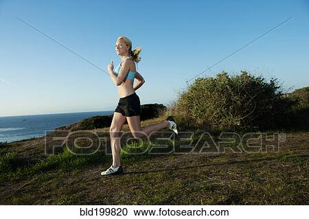 Stock Image - Caucasian woman running near ocean. Fotosearch