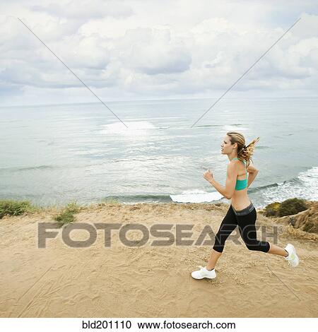 Stock Image - Caucasian woman running on beach. Fotosearch