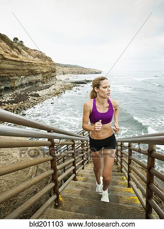 Stock Image - Caucasian woman running up stairs next to ocean. Fotosearch
