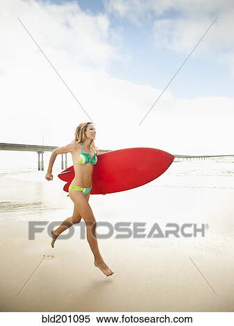 Stock Photography - Caucasian woman running with surfboard. Fotosearch