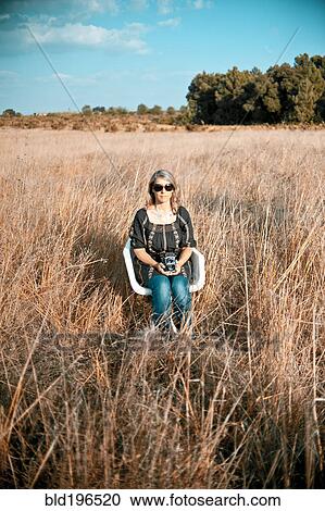 Stock Image - Caucasian woman sitting in field with old-fashioned camera. Fotosearch