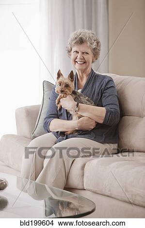 Picture - Caucasian woman sitting on sofa holding dog. Fotosearch
