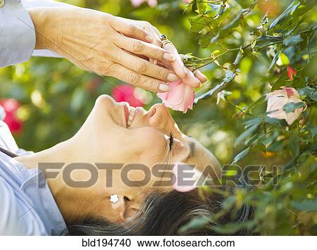 Stock Image - Caucasian woman smelling flower outdoors. Fotosearch