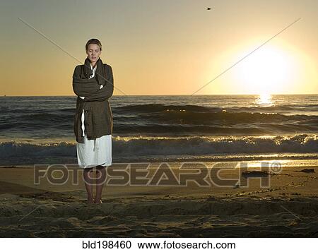 Stock Image - Caucasian woman standing on beach at sunset. Fotosearch