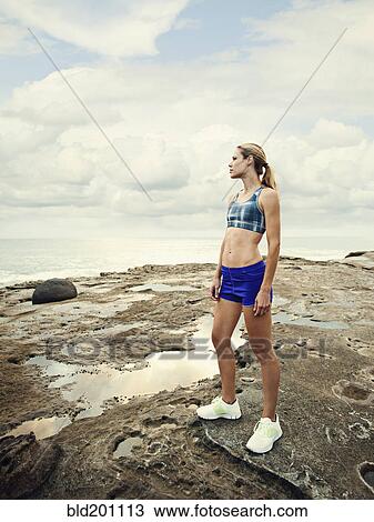 Stock Image - Caucasian woman standing on rocks near beach. Fotosearch