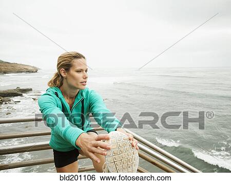 Stock Photograph - Caucasian woman stretching before exercise next to ocean. Fotosearch