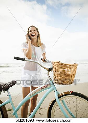 Stock Image - Caucasian woman using cell phone on beach. Fotosearch