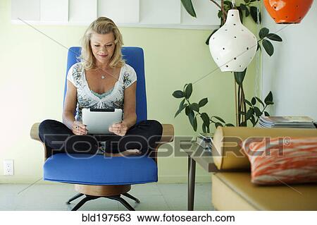Stock Image - Caucasian woman using digital tablet in living room. Fotosearch