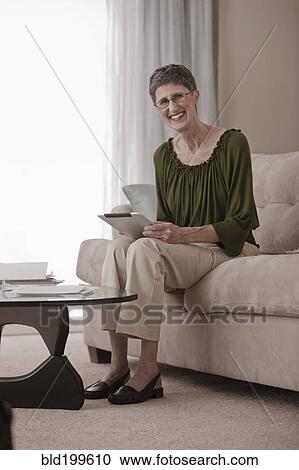 Stock Image - Caucasian woman using digital tablet on sofa. Fotosearch