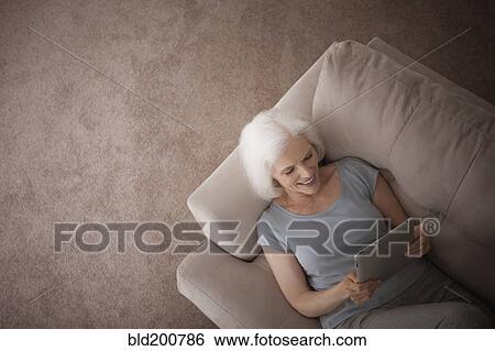 Stock Photograph - Caucasian woman using digital tablet on sofa. Fotosearch