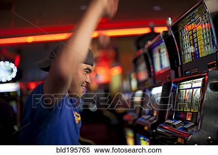 Stock Photography - Cheering Native American man playing slot machines in casino. Fotosearch