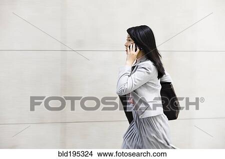 Picture - Chinese businesswoman walking and talking on cell phone. Fotosearch