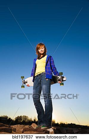 Chinese girl standing on rocks holding skateboard View Large Photo Image Stock Photo - Chinese girl standing on rocks holding skateboard. Fotosearch