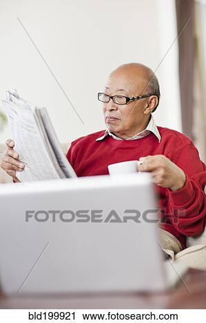 Stock Image - Chinese man reading newspaper and drinking coffee. Fotosearch