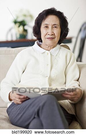 Stock Image - Chinese woman on sofa reading book. Fotosearch