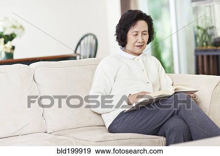 Stock Photo - Chinese woman on sofa reading book. Fotosearch
