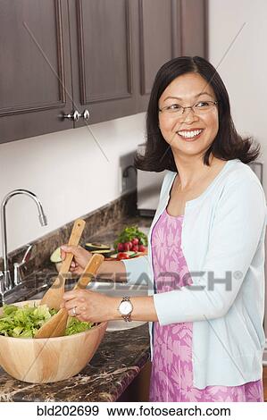 Stock Photo - Chinese woman tossing salad in kitchen. Fotosearch