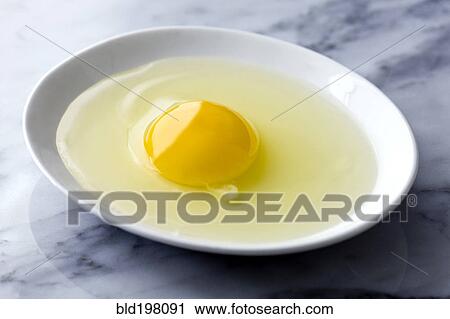 Stock Image - Close up of raw egg in bowl. Fotosearch