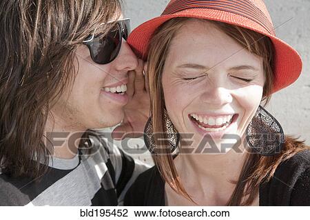 Stock Image - Close up of teenage boy whispering in smiling girl's ear. Fotosearch