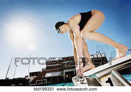 Stock Image - Competitive swimmer crouching on starting block. Fotosearch