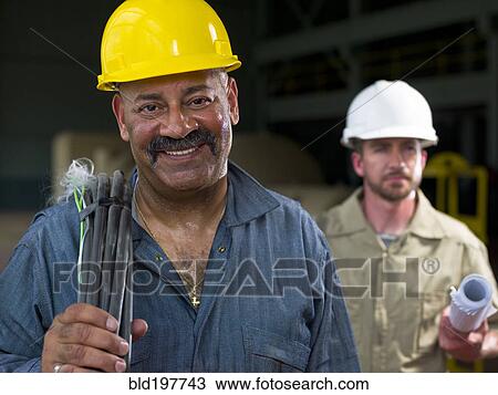Stock Image - Construction workers holding blueprints and cable. Fotosearch