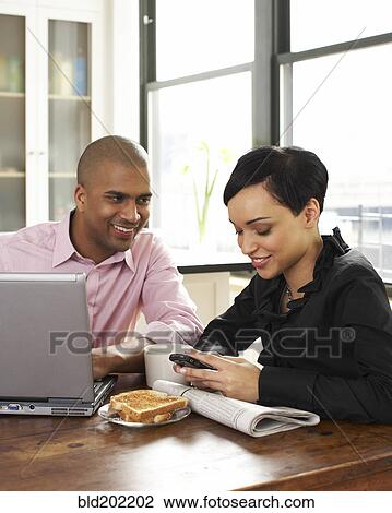 Stock Image - Couple eating breakfast and using laptop and cell phone. Fotosearch