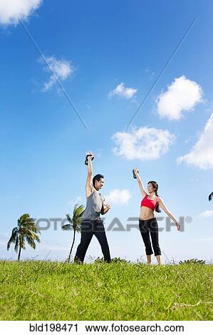 Stock Image - Couple exercising together in field. Fotosearch