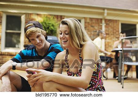 Stock Image - Couple hanging out together on patio looking at cell phone. Fotosearch