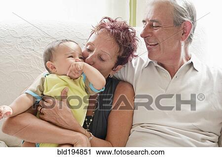 Stock Image - Couple holding baby on sofa. Fotosearch