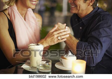 Stock Image - Couple holding hands over coffee in restaurant. Fotosearch