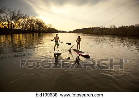 Stock Photo - Couple paddling in river on surfboards. Fotosearch