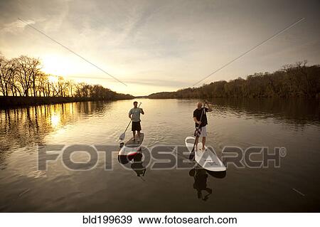 Stock Photo - Couple paddling in river on surfboards. Fotosearch