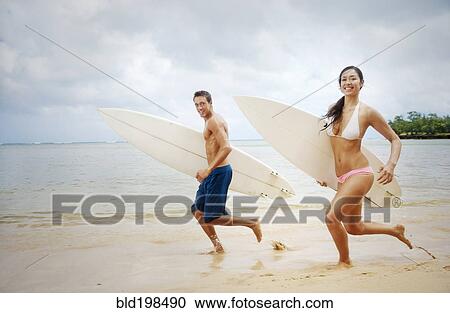 Couple running on beach carrying surfboards View Large Photo Image Stock Image - Couple running on beach carrying surfboards. Fotosearch