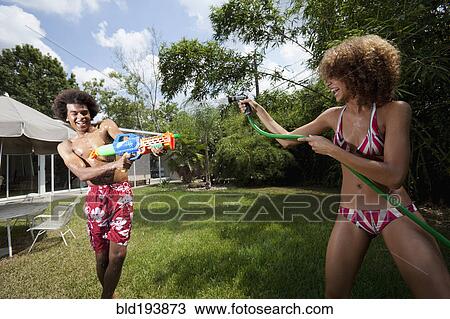 Stock Image - Couple squirting each other with water in backyard. Fotosearch