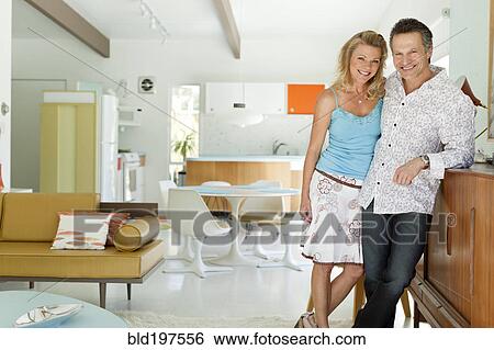 Couple standing together in living room View Large Photo Image Stock Photograph - Couple standing together in living room. Fotosearch