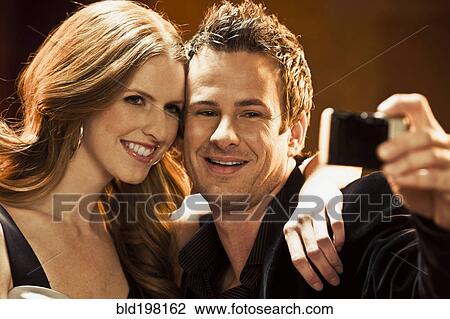 Stock Image - Couple taking self-portrait with camera in nightclub. Fotosearch