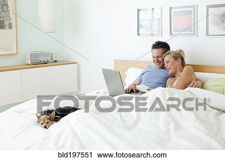 Stock Image - Couple using laptop together in bed. Fotosearch