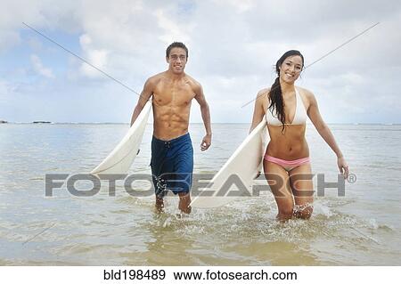 Stock Photo - Couple walking in ocean carrying surfboards. Fotosearch