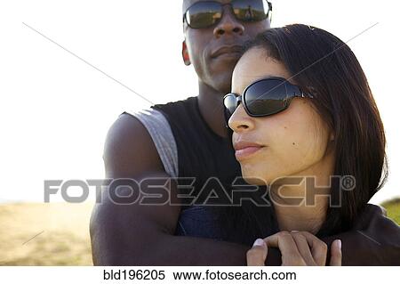 Stock Photography - Couple wearing sunglasses hugging outdoors. Fotosearch