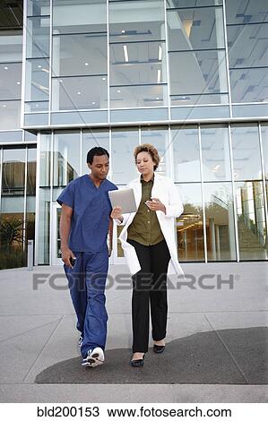 Stock Image - Doctor and co-worker looking at digital tablet. Fotosearch