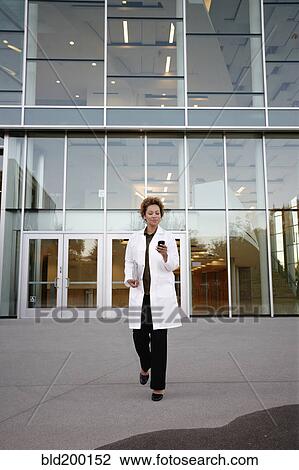 Stock Image - Doctor walking and text messaging on cell phone. Fotosearch