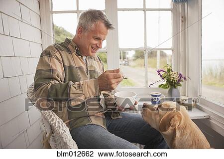 Stock Image - Dog watching Caucasian man eating breakfast. Fotosearch