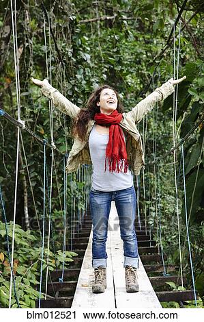 Stock Image - Excited woman walking on suspension bridge. Fotosearch