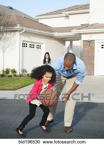Stock Image - Father and daughter playing basketball in road. Fotosearch