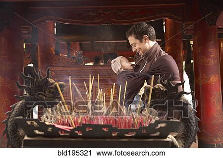 Stock Image - Father carrying baby in sling in temple. Fotosearch