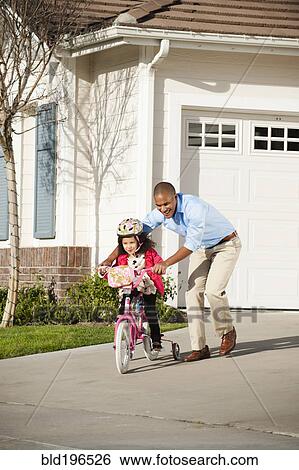 Stock Photograph - Father helping daughter learn to ride a bike. Fotosearch