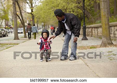 Father helping daughter ride bicycle on sidewalk View Large Photo Image Stock Photo - Father helping daughter ride bicycle on sidewalk. Fotosearch