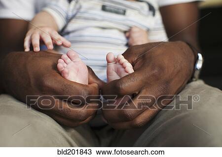 Stock Image - Father holding baby's small feet. Fotosearch