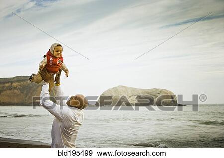 Stock Photo - Father lifting baby son overhead at beach. Fotosearch