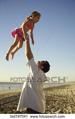 Stock Image - Father lifting daughter in air on beach. Fotosearch